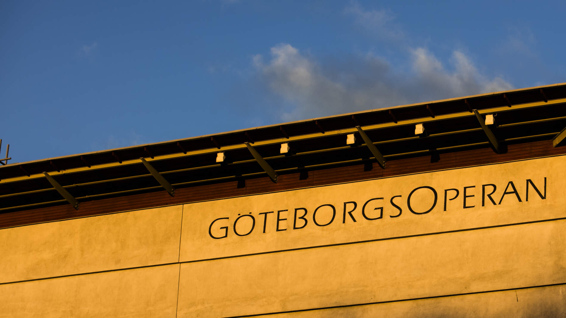 Översta delen av Göteborgsoperans fasad, upplyst i morgonsolen. Ordet "GöteborgsOperan" syns skrivet på fasaden.