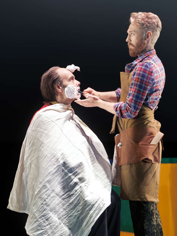 Figaro står framför Doktor Bartolo som sitter i en barberstol. Bartolo har raklödder på kinderna och en stor klick i pannan.