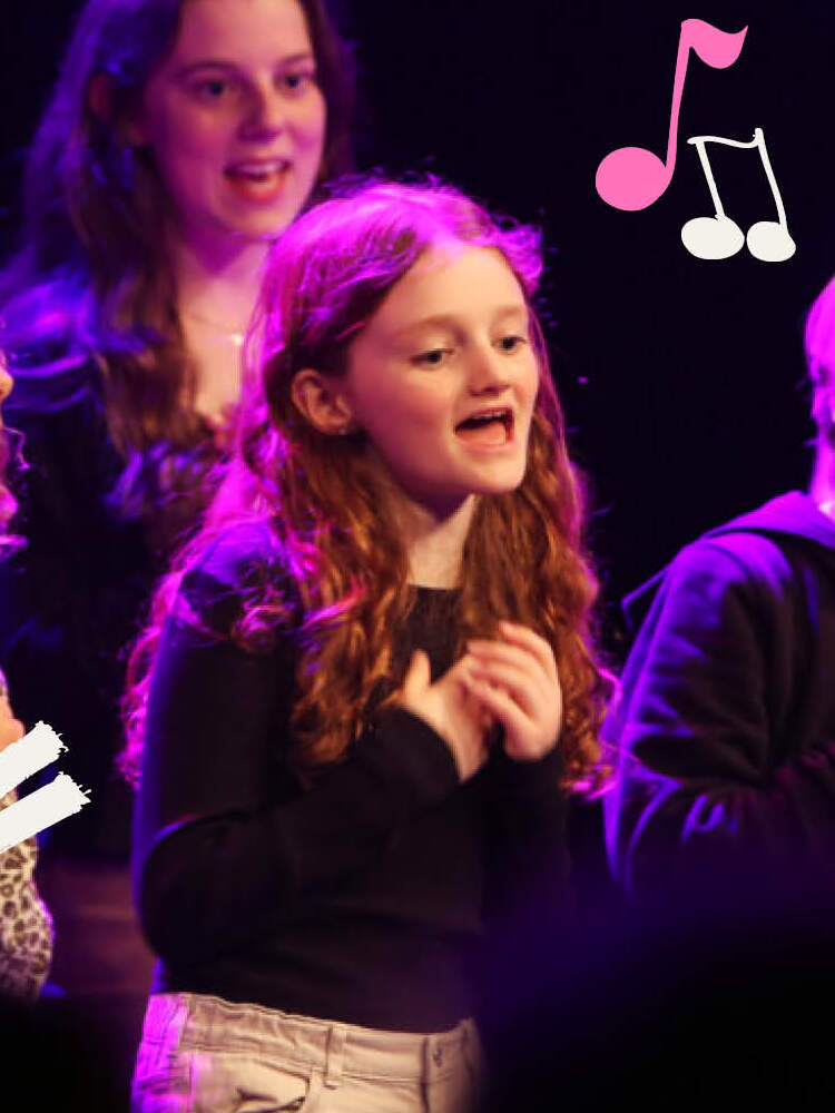 En grupp barn står och sjunger under rosa ljus. De har armarna korsade framför sig med händerna placerade över hjärtat.