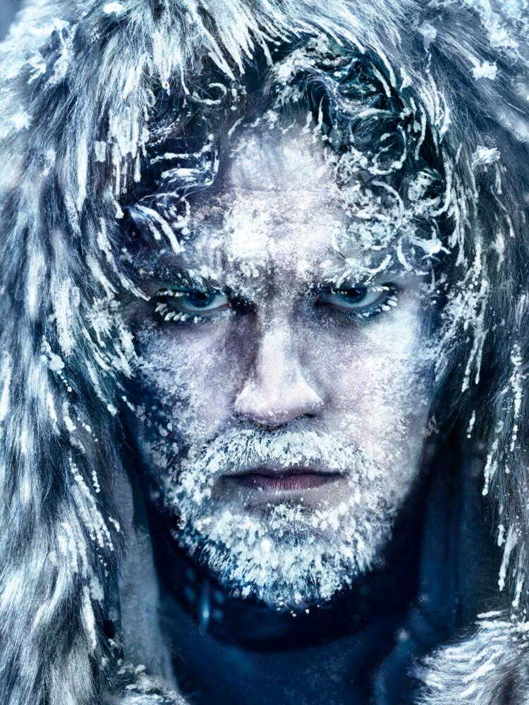Närbild av en skäggig mans ansikte. Han bär en pälshuvudbonad och stirrar in i kameran. Snö finns i skägget och på hatten.