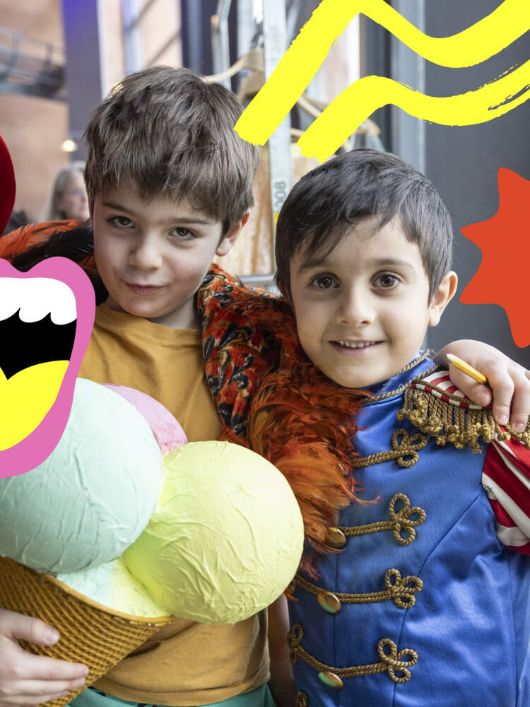 Tre barn står i en teaterfoajé med armarna om varandras axlar. De bär och håller i olika scenkostymer och rekvisita.