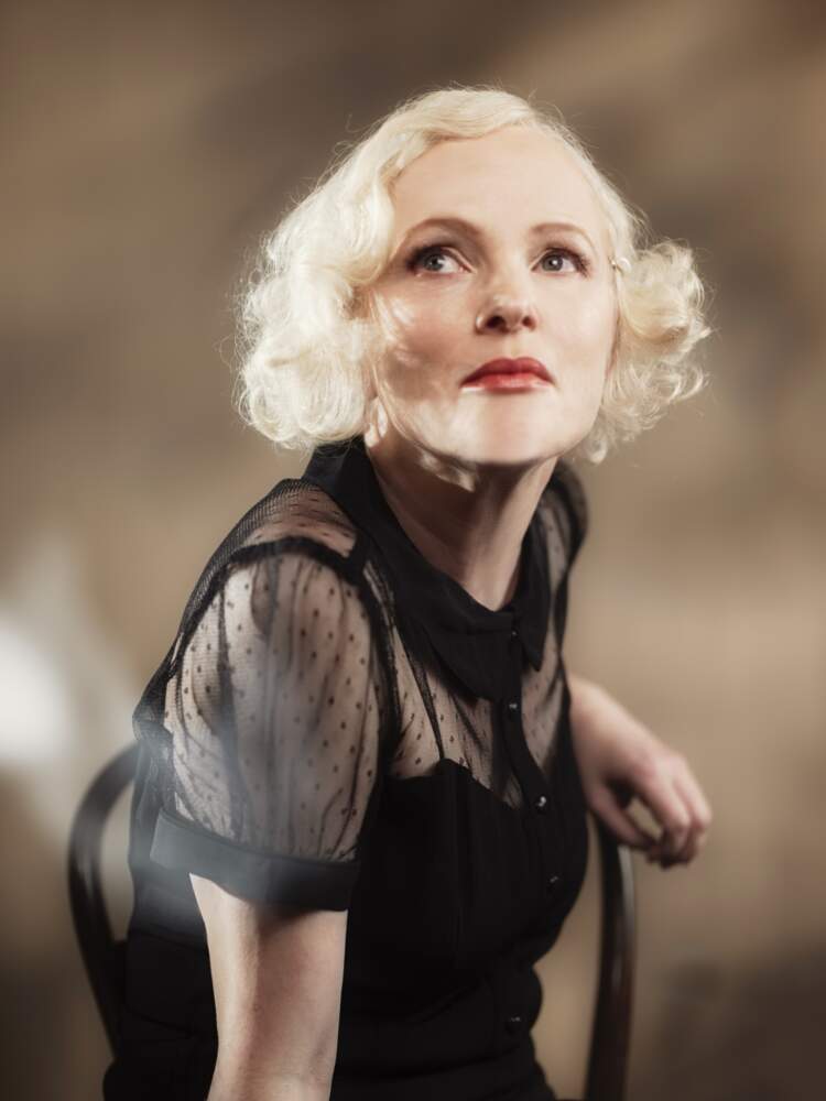 Manon sitter i en stol och tittar upp till höger om henne. Rummet bakom henne är oskarp.