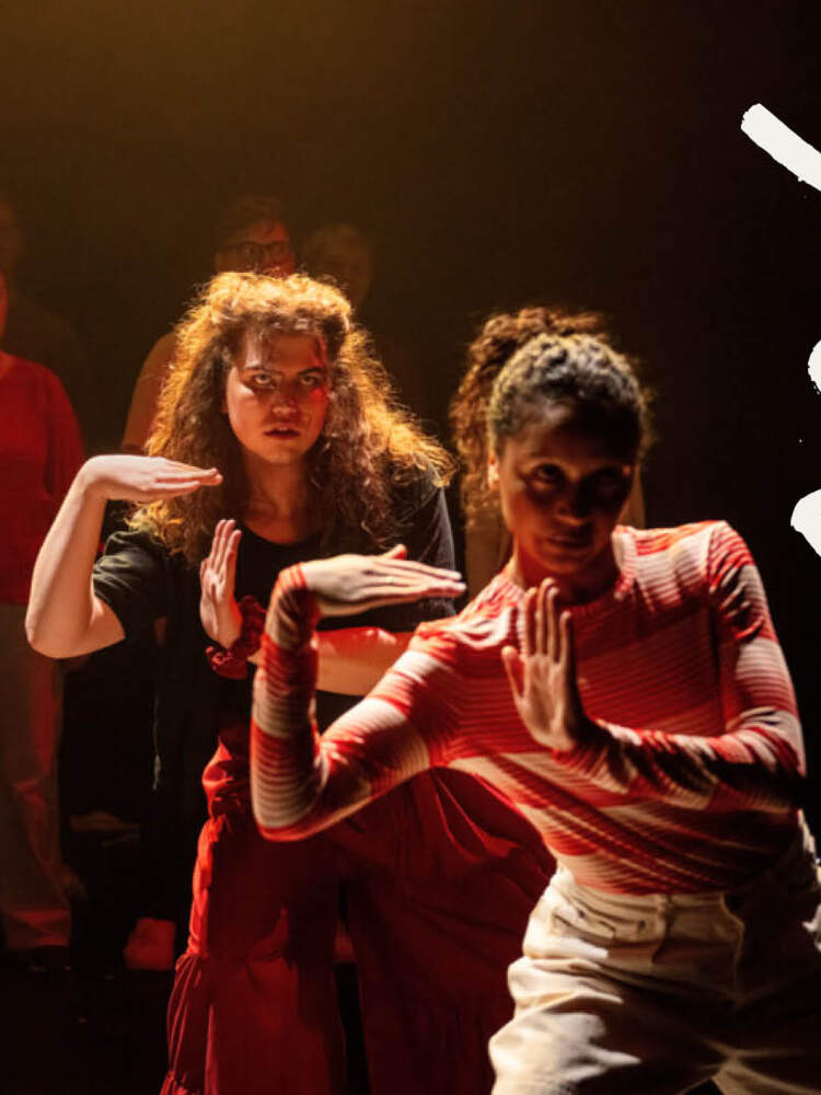 Två ungdomar under en spotlight gör ett utfall och gestikulerar åt höger. Bakom dem står två rader människor i skuggorna.