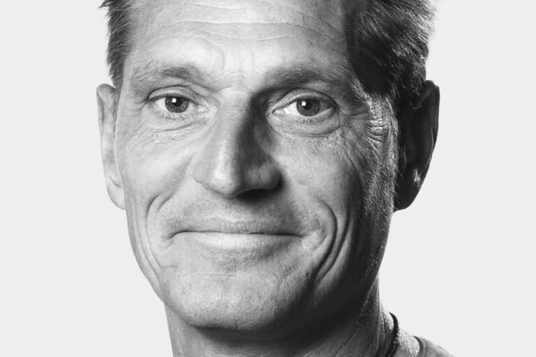En svartvit bystporträttfoto av en man som sitter framför en ljus fond. Han tittar in i objektivet mot betraktaren. En svartvit bystporträttfoto av en man som sitter framför en ljus bakgrundsfond. Han tittar in i objektivet mot betraktaren.