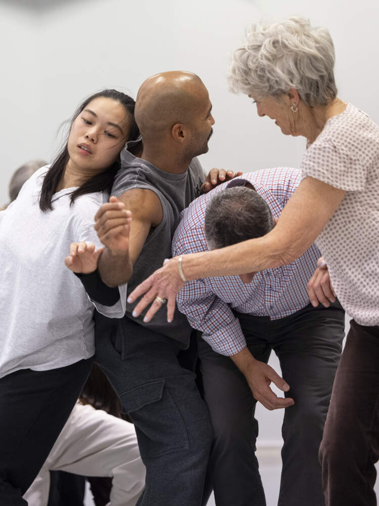 En grupp äldre och yngre vuxna rör sig tätt tillsammans med armarna höjda, några med ryggarna lutade mot varandra.