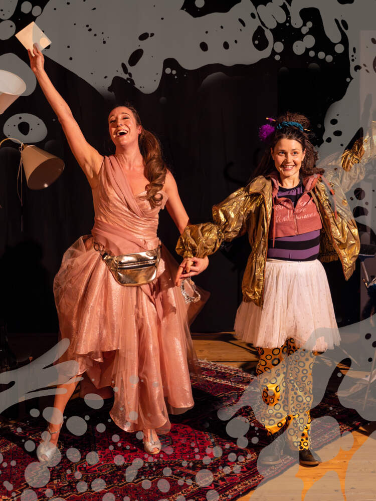 Två skådespelare står och håller hand, med andra armarna upplyfta. En skådespelare sjunger med slutna ögon och den andra ler.