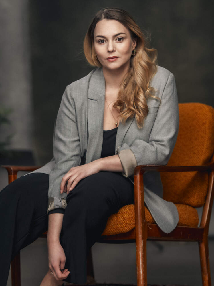 En operasolist sitter i en fåtölj, lutar sig framåt och tittar mot kameran.