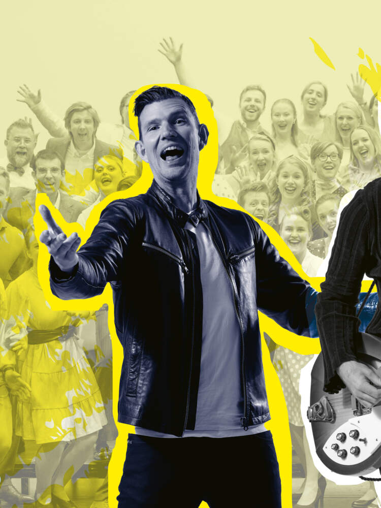 Två män med gitarrer står och sjunger entusiastiskt med en skara körmedlemmar bakom sig.