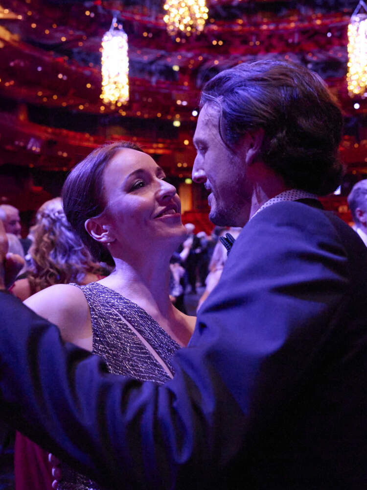 Ett par valsar i en rödbelyst salong, själva upplysta av lila ljus. Andra par valsar bakom dem. Ljuskronor hänger från taket.