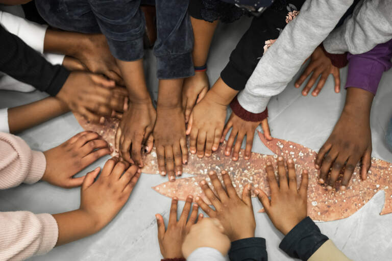 En grupp barnhänder sträcker sig ut med palmerna vilande platt på ett tecknat vargsvans som ligger på golvet.