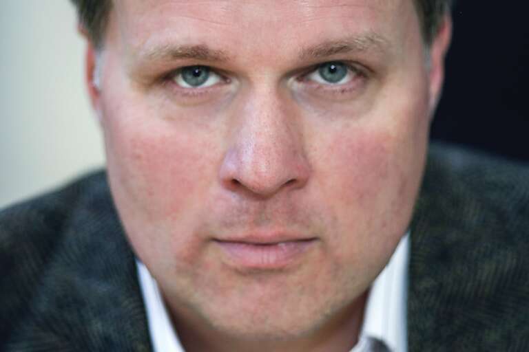 En porträttbild av någon som sitter och tittar in i kameran.