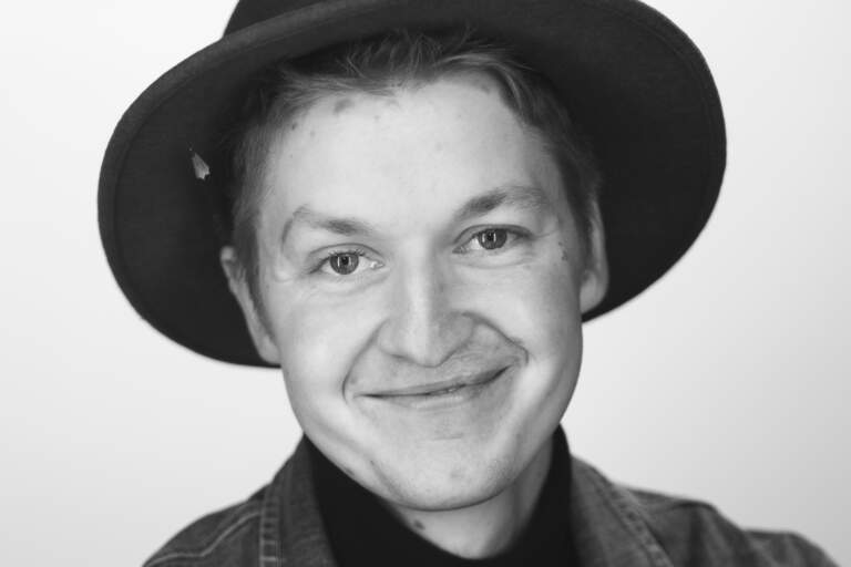 En svartvit bystporträttfoto av en man som sitter framför en ljus fond. Han tittar in i objektivet mot betraktaren. En svartvit bystporträttfoto av en man som sitter framför en ljus bakgrundsfond. Han tittar in i objektivet mot betraktaren.