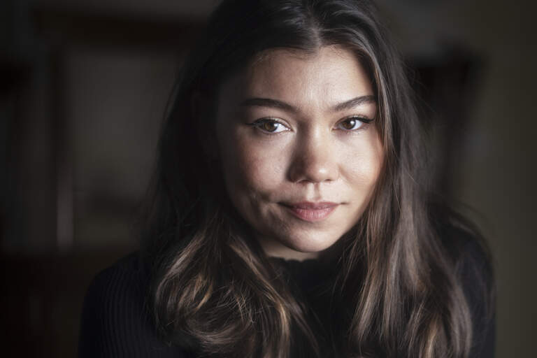 En musikartist sitter i ett mörkt rum och tittar in i kameran med neutralt ansiktsuttryck. Hon är belyst från vänster sida.