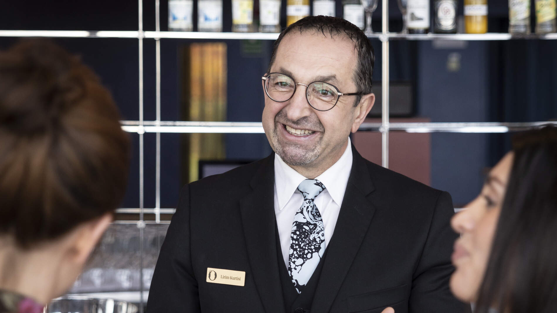 En leende caféchef pratar med två kunder som står vid cafédisken och köper kaffe och något att äta.