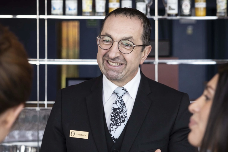 En leende caféchef pratar med två kunder som står vid cafédisken och köper kaffe och något att äta.