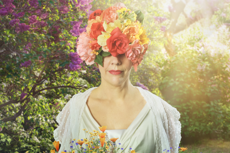 En person som bär en huvudbonad täckt av färgglada blommor står bland blommor i en solig, frodig trädgård.
