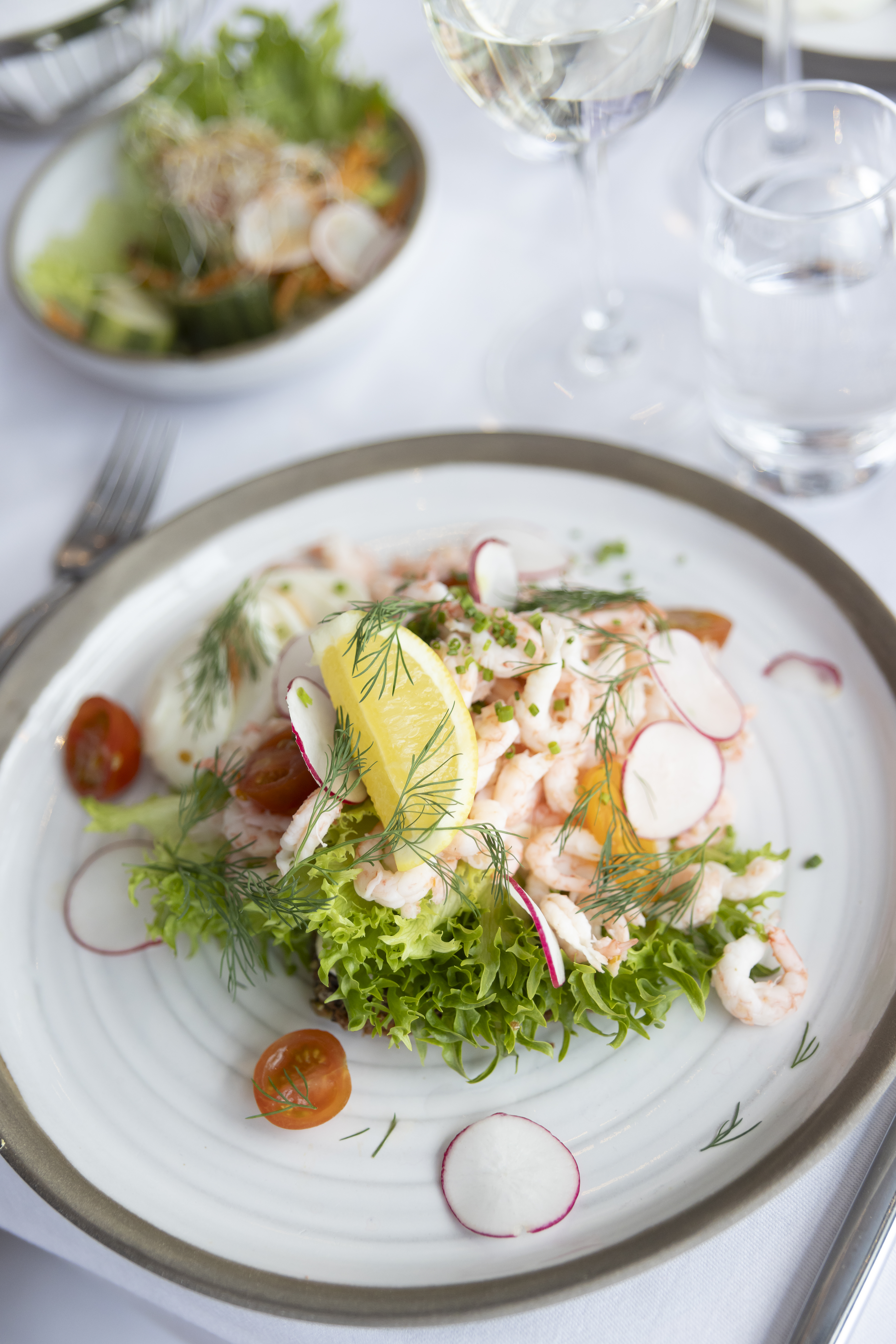 Närbild på en räkmacka med citron, dill, rädisor och mera - uppdukat fint på ett bord.