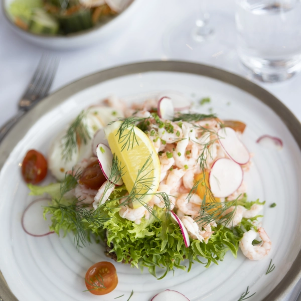 Närbild på en räkmacka med citron, dill, rädisor och mera - uppdukat fint på ett bord.