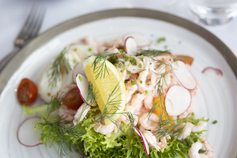 Närbild på en räkmacka med citron, dill, rädisor och mera - uppdukat fint på ett bord.