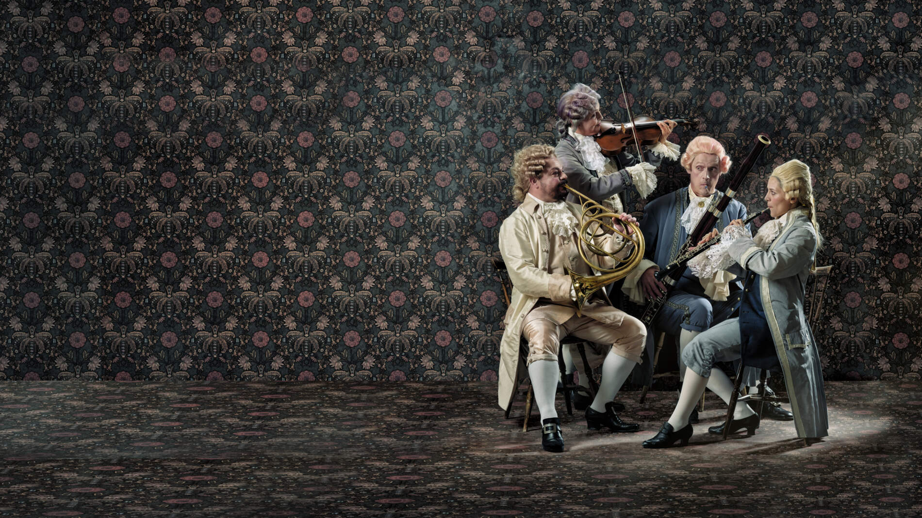 En kvartett musiker spelar sina instrument i ett tapetserat rum, alla iklädda sidenkläder och peruker från 1700-talet.