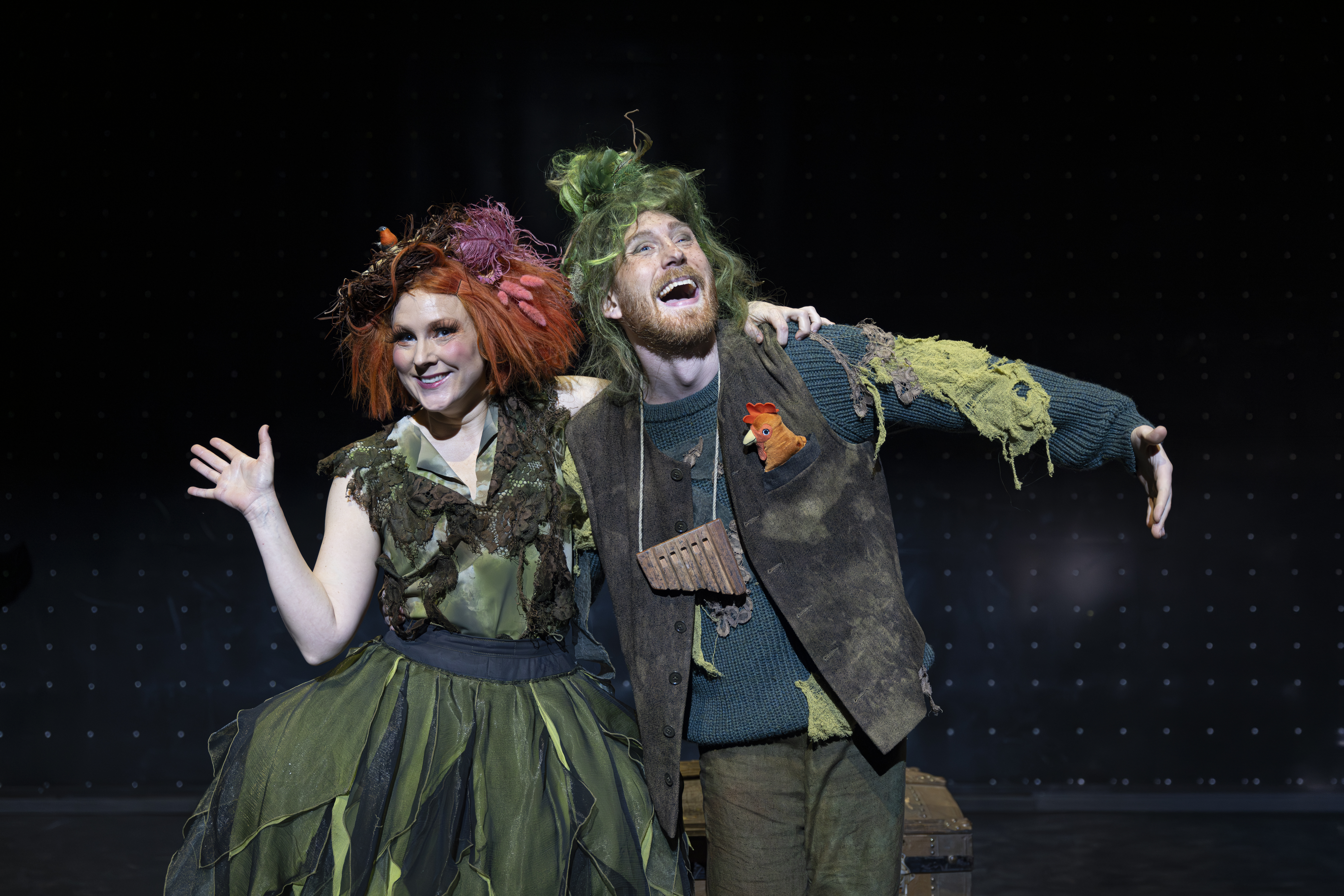 Papageno står med armen om Papagena, som vinkar. Båda ler.