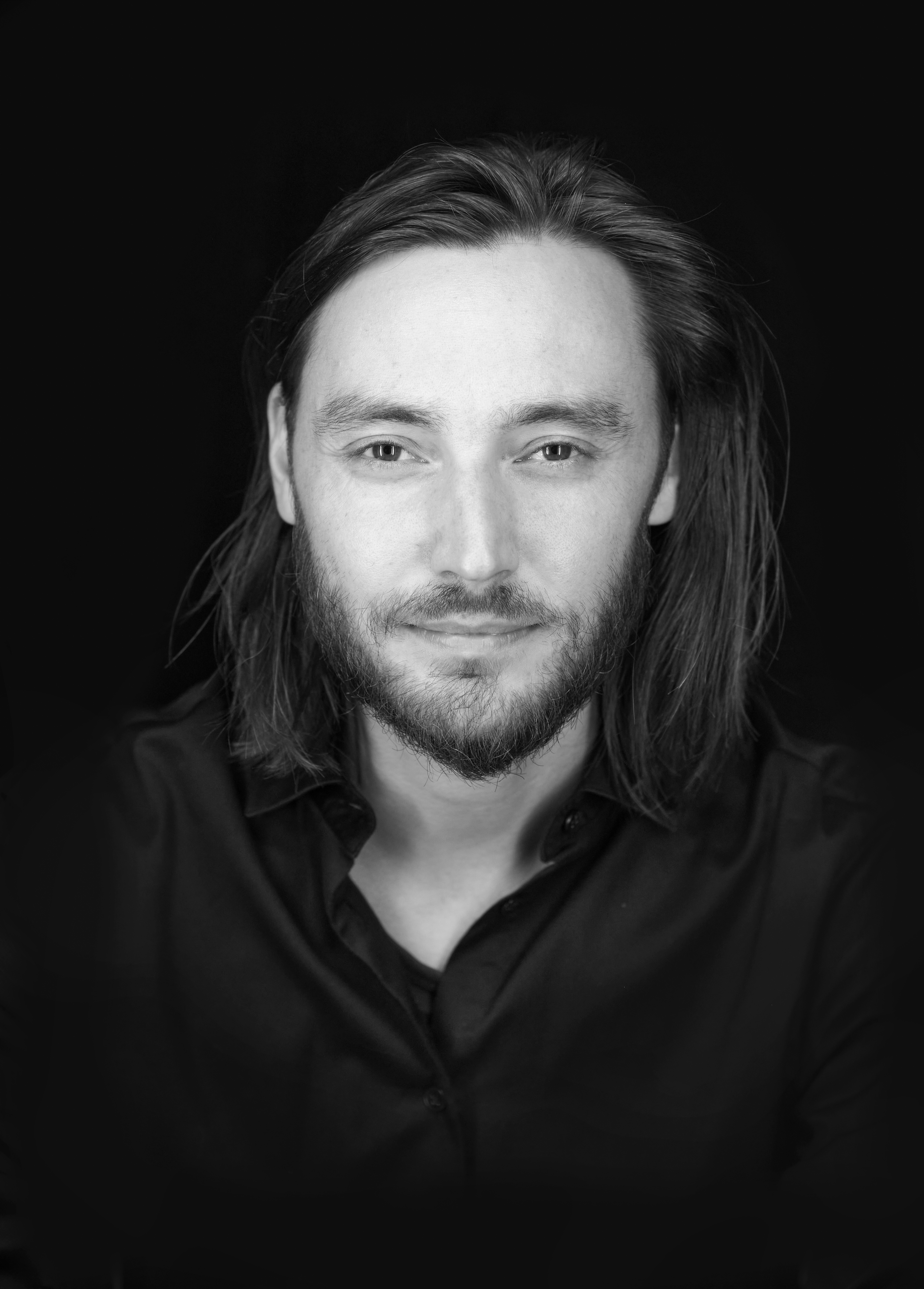 En svartvit bystporträttfoto av någon som sitter framför en svart fond.