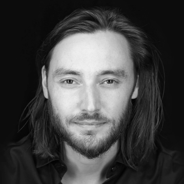 En svartvit bystporträttfoto av någon som sitter framför en svart fond.