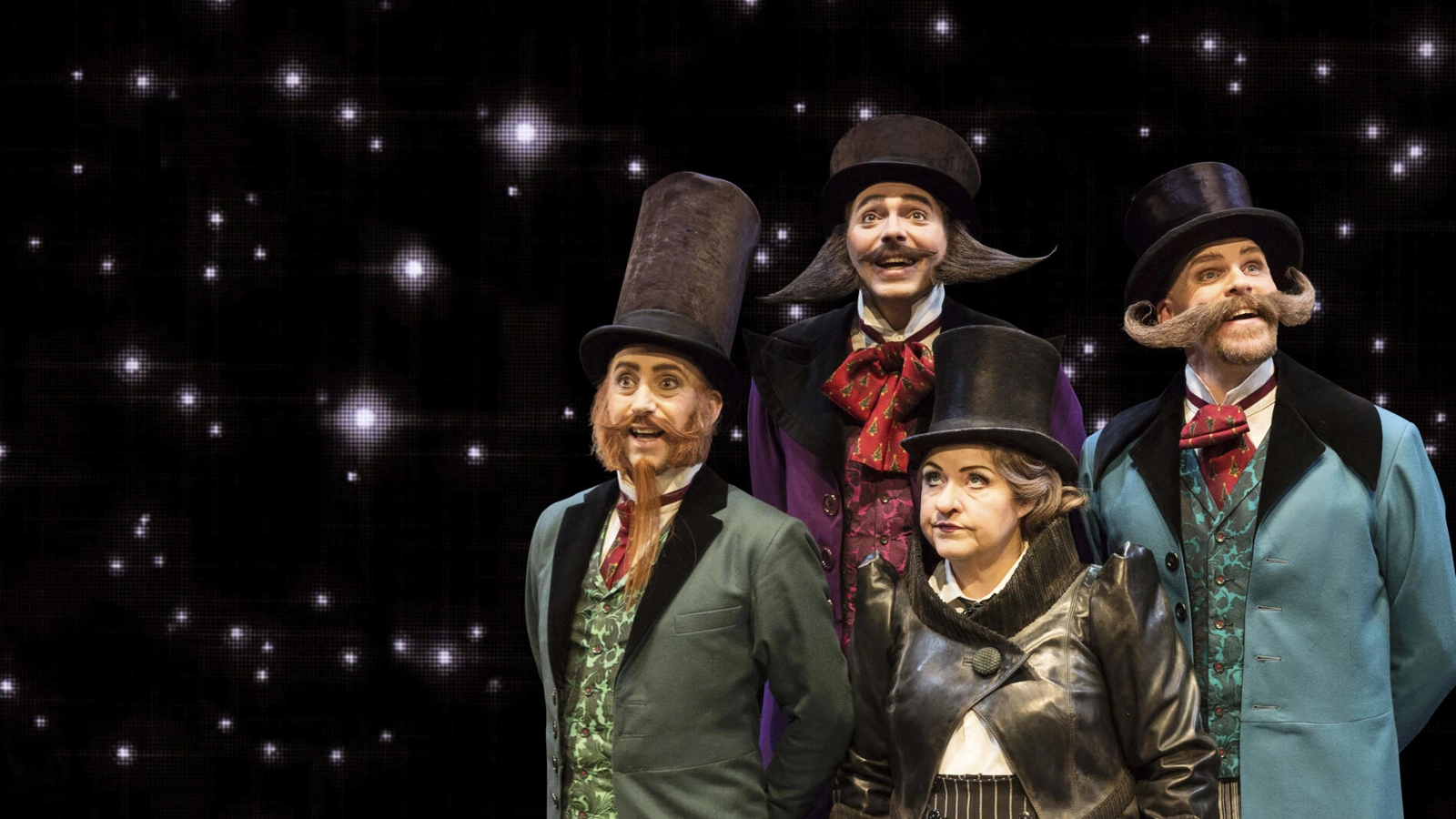 De tre berättarna står leende i en grupp runt Scrooge, som himlar med ögonen.