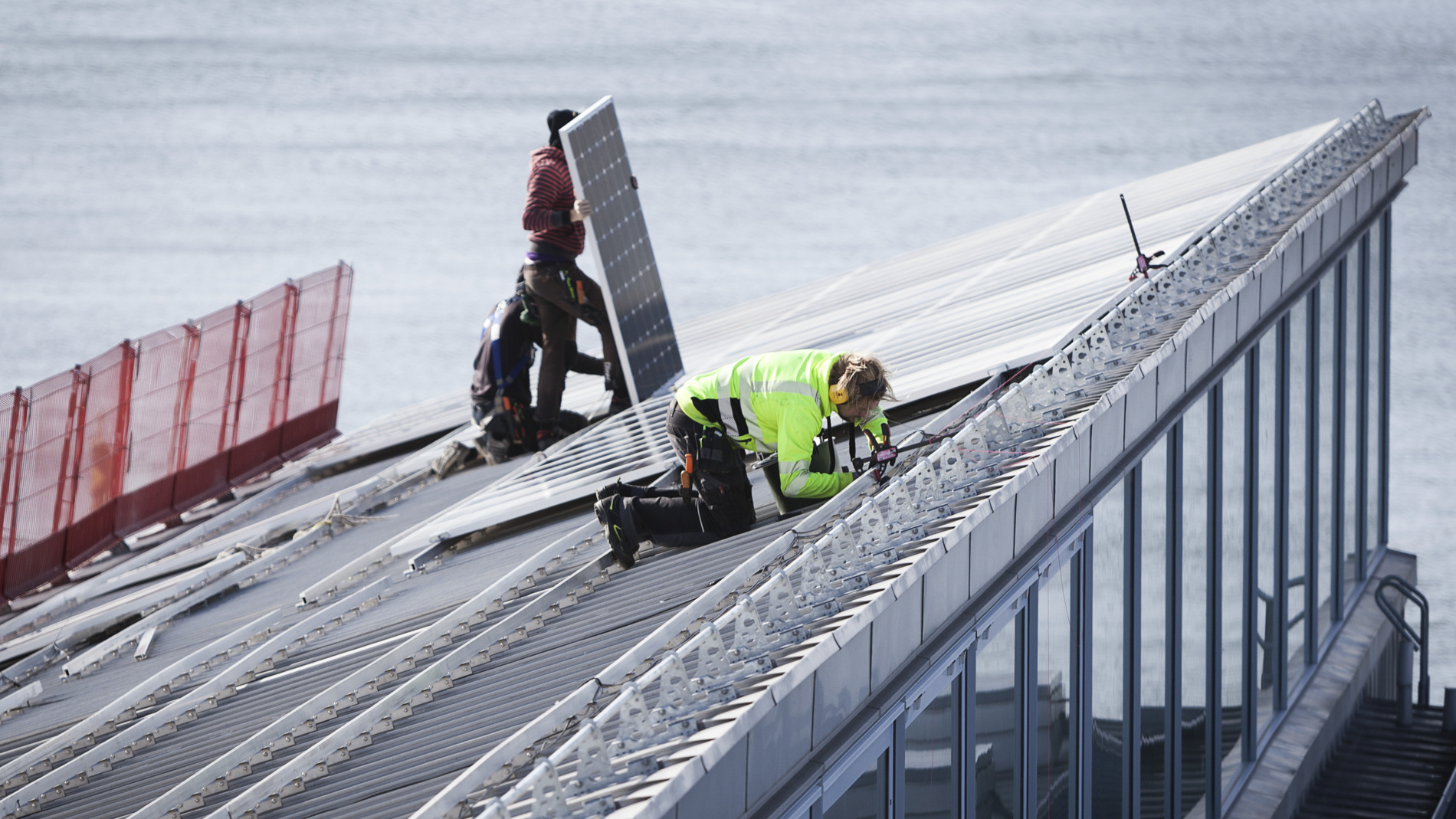 Tre tekniker installerar solpaneler på det sluttande taket på ett operahus.