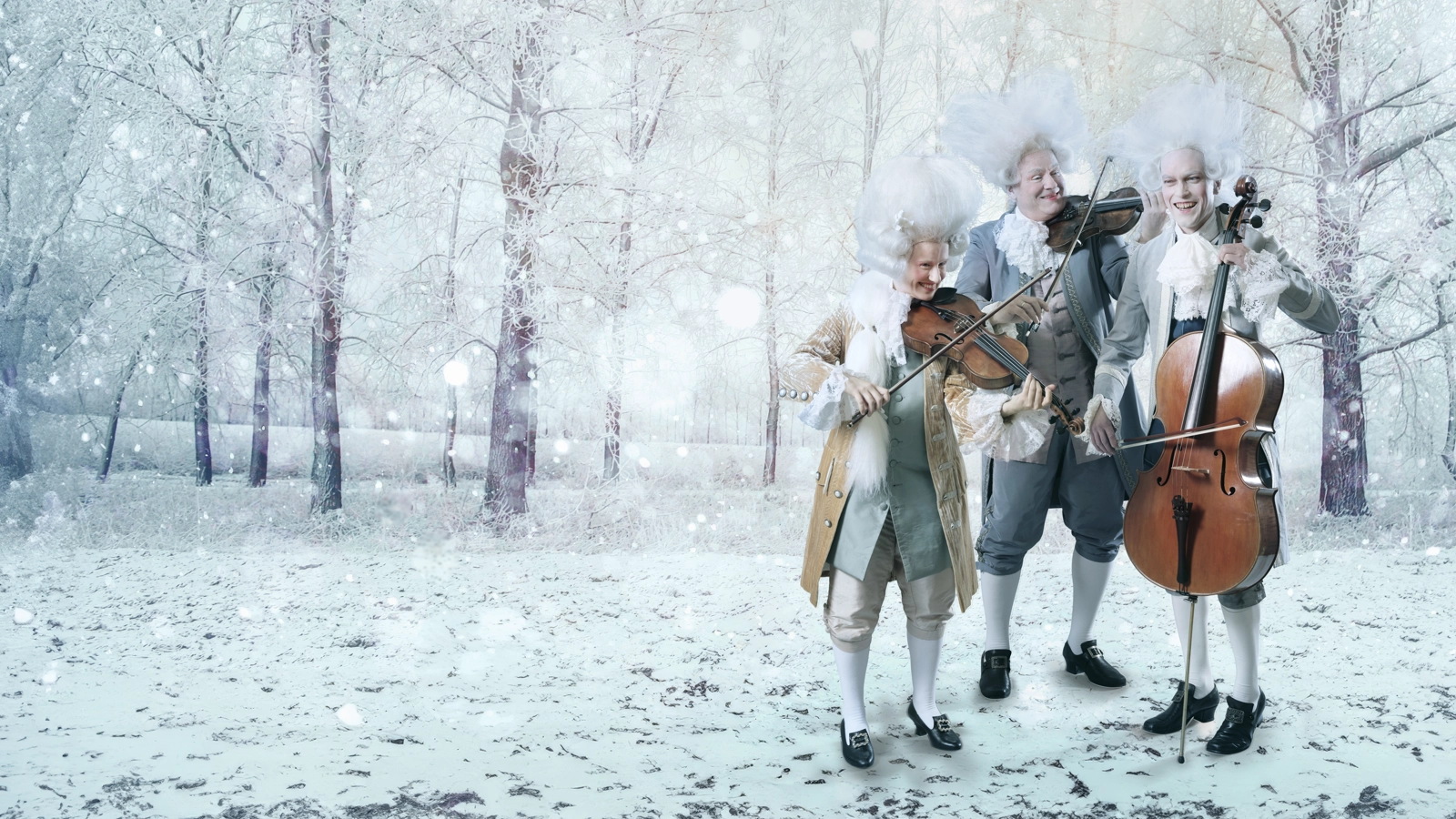Tre stråkmusiker i barocka kläder och stora vita peruker står och spelar sina instrument på ett snöigt fält omringad av träd.