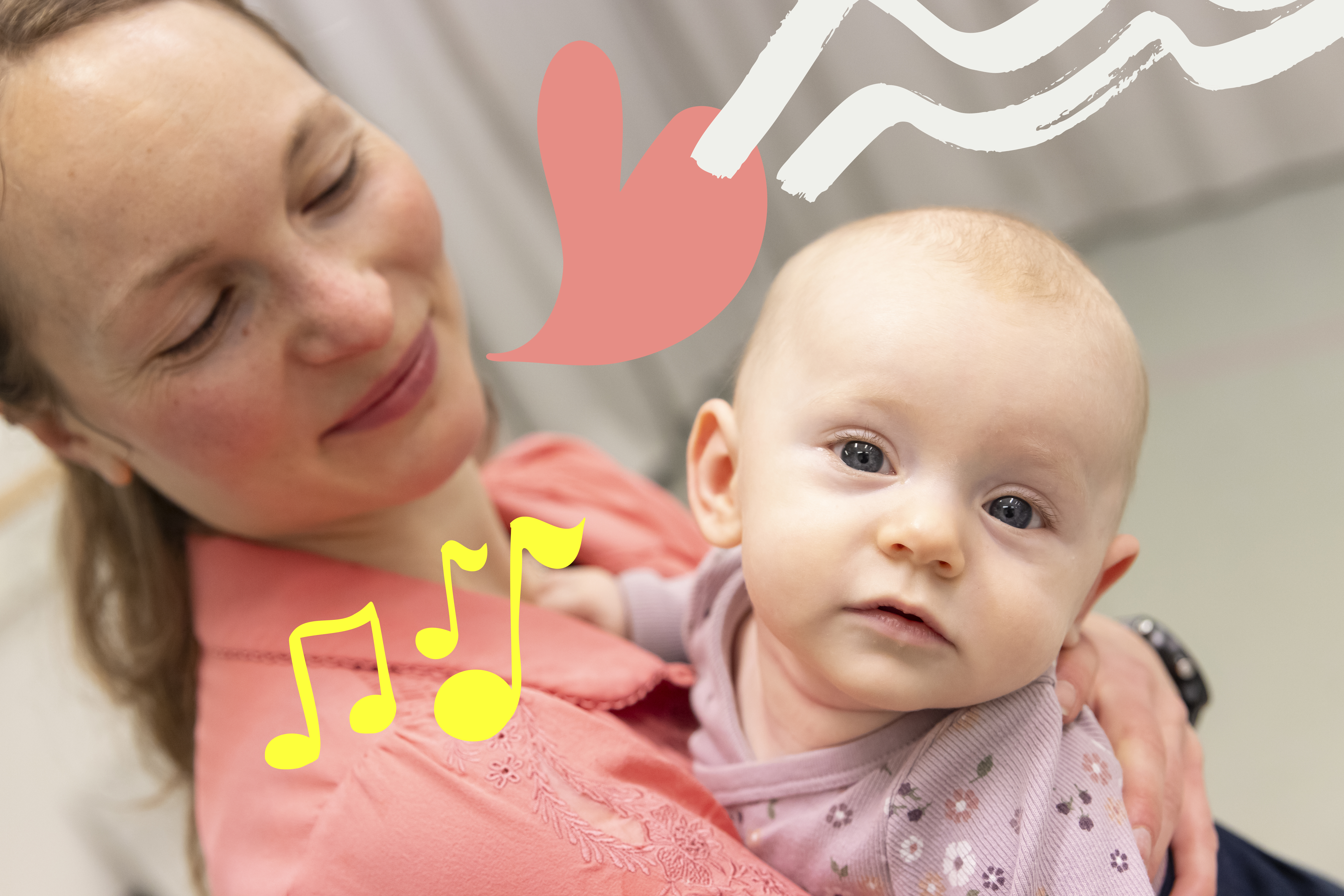 En ung bebis som hålls av sin mamma tittar rakt in i kameran. Hennes mamma tittar på henne och ler.