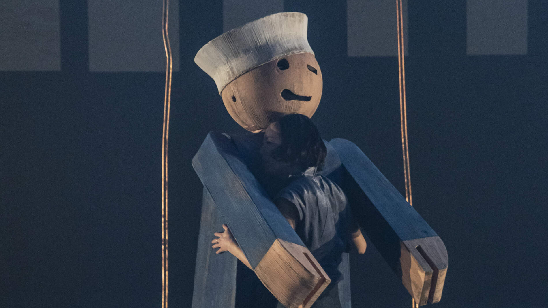 En dansare står och omfamnar en gigantisk träfigur av en blinkande leksakssjöman som är ett huvud längre än henne.