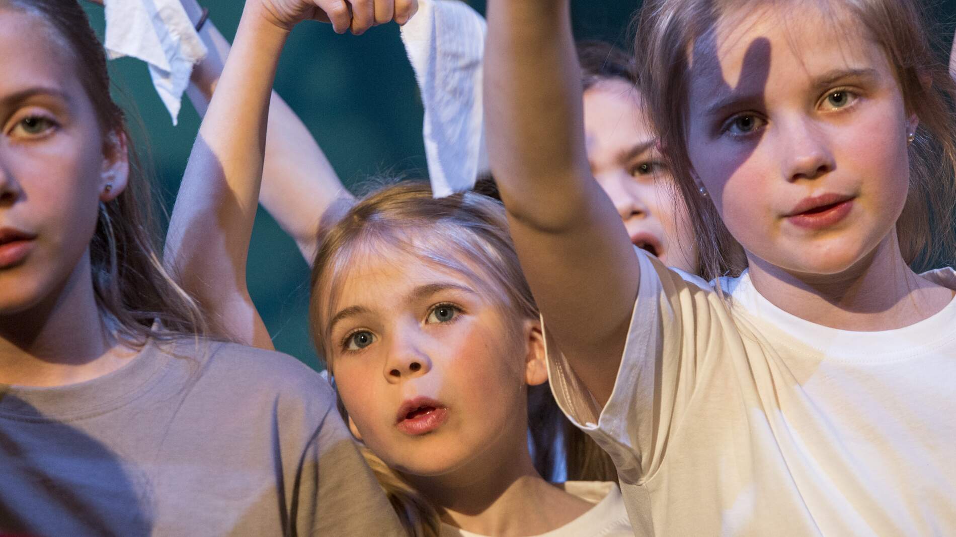 Flera barn i grå eller vita t-shirts står och sjunger och håller upp sin högra arm.