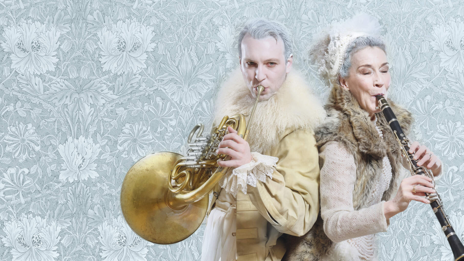 En hornist och klarinettist står rygg mot rygg med sina instrument mot en ljusblå fond. De har frost i håret och pälskappor.