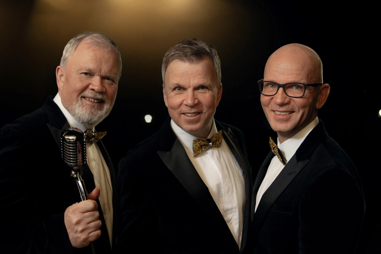 Tre leende bröder står upplyst på en mörk scen. De diggar faktumet att ett par gyllene dojor står och blixtar bakom kameran.