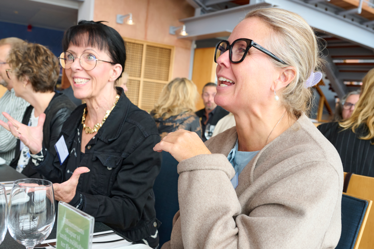 Flera personer sitter vid ett restaurangbord, ler och samtalar.