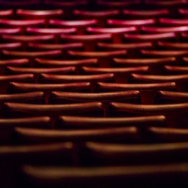 Fällstolar av röda sammet står i långa böjda rader i en stor teater auditorium.