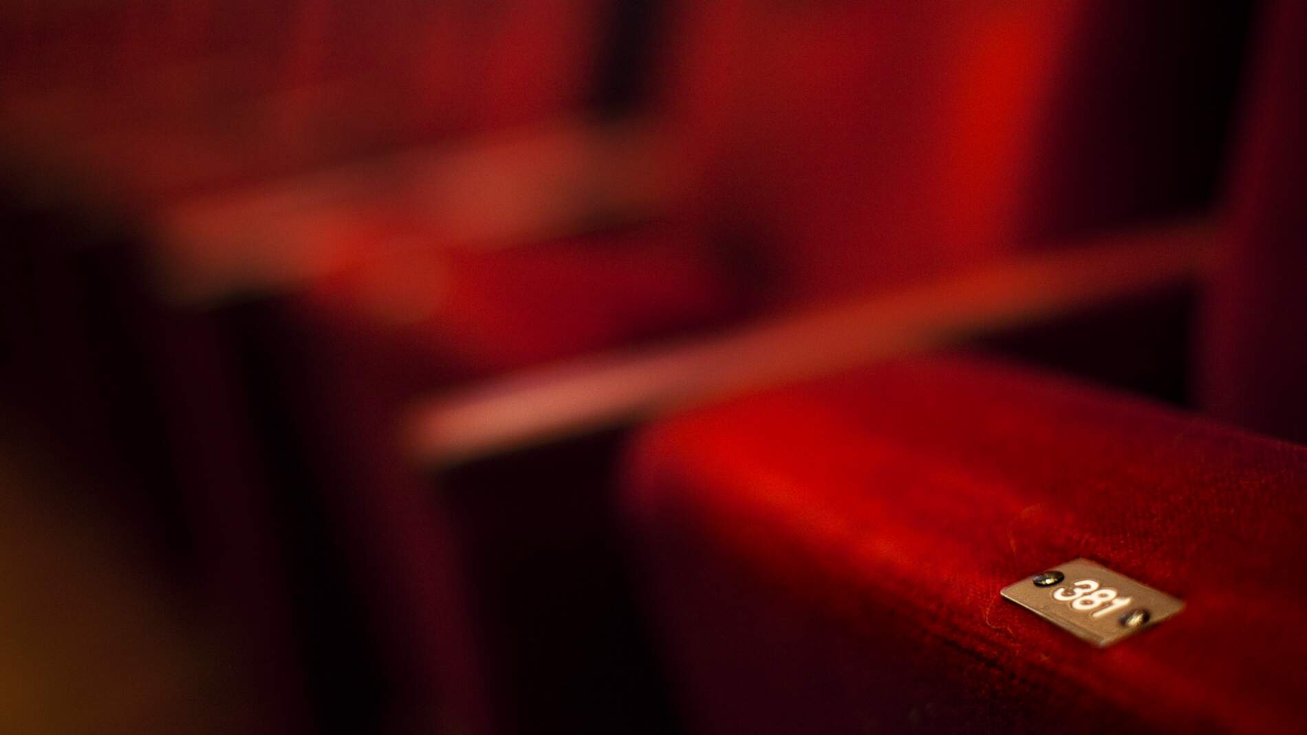 En närbild av en hopfällbar teaterstol klädd i röd sammet. Sitsen har siffran 381.