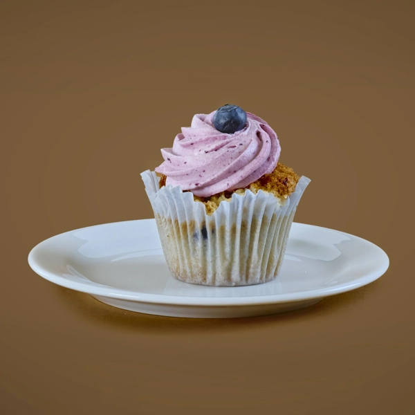 En cupcake med rosa frosting och ett blåbär ovanpå ligger på en liten tallrik.