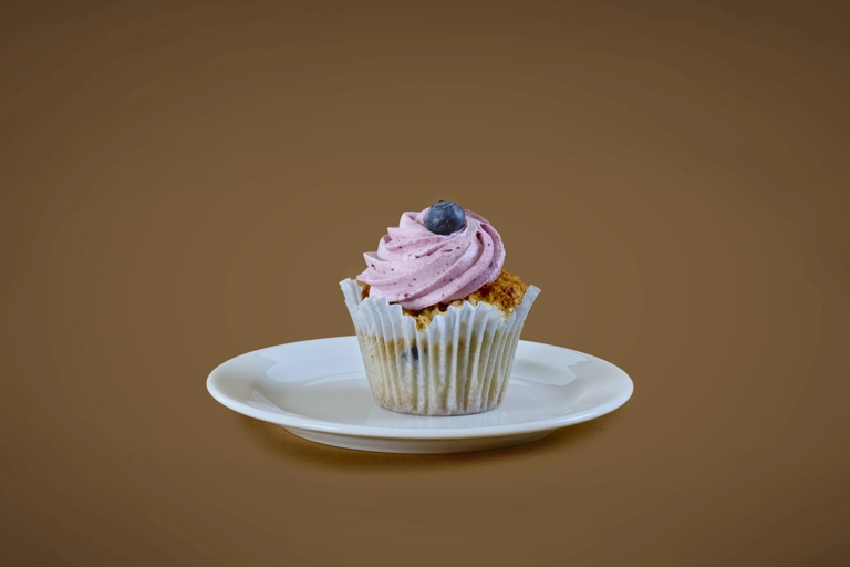 En cupcake med rosa frosting och ett blåbär ovanpå ligger på en liten tallrik.