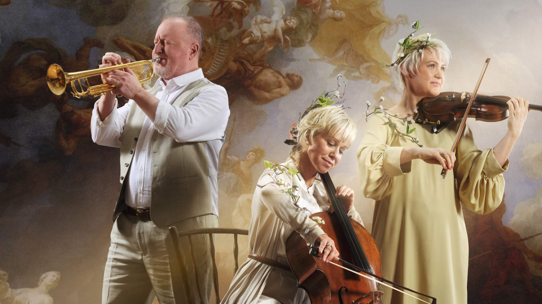 En cellist, violast och trumpetist spelar sina instrument mot en målad barockbakgrund. Två har lövkransar i håret.