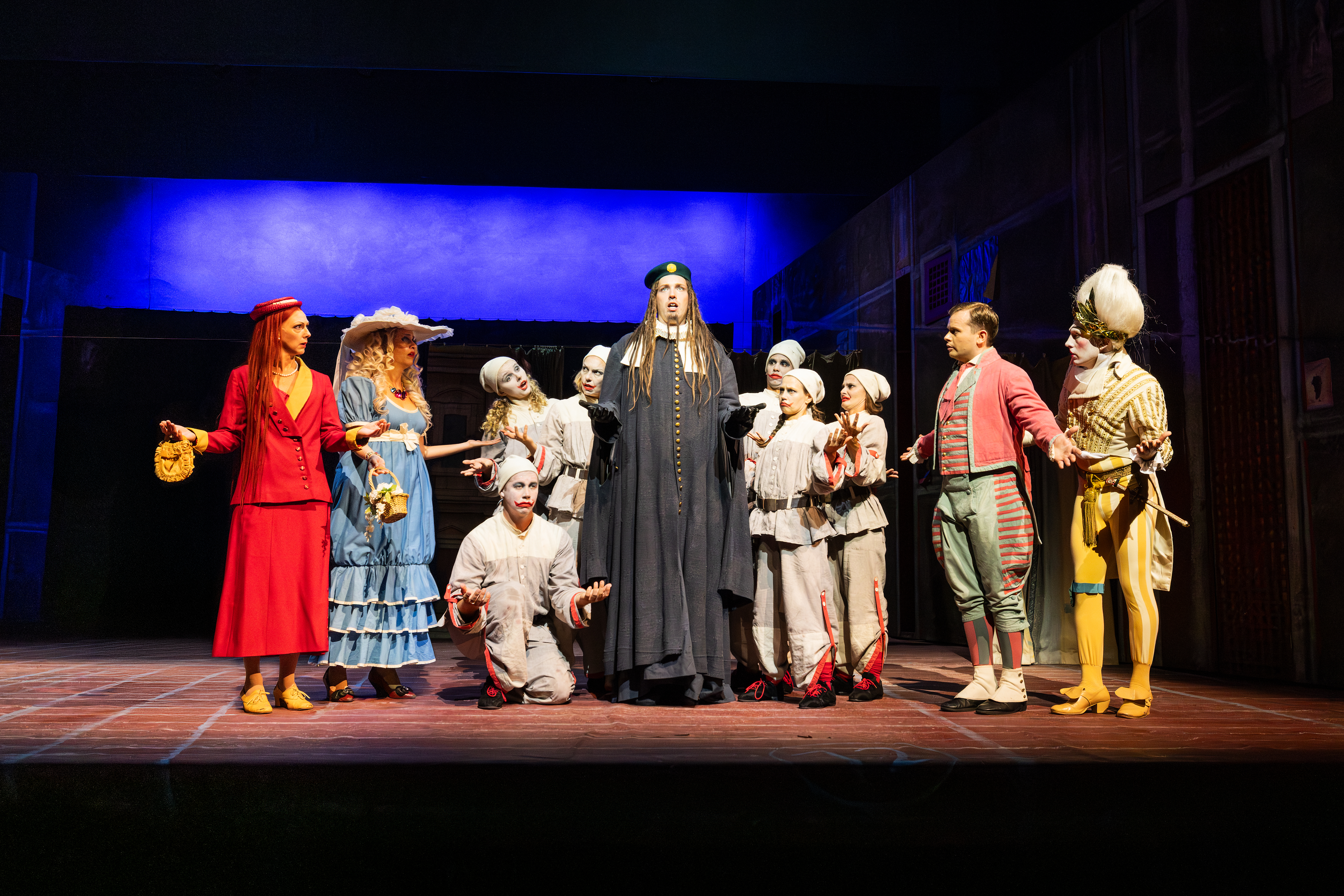 Alidoro står och sjunger mitt i en grupp, inklusive Clorina, Thisbe, Don Ramiro, Dandini och några clowner.