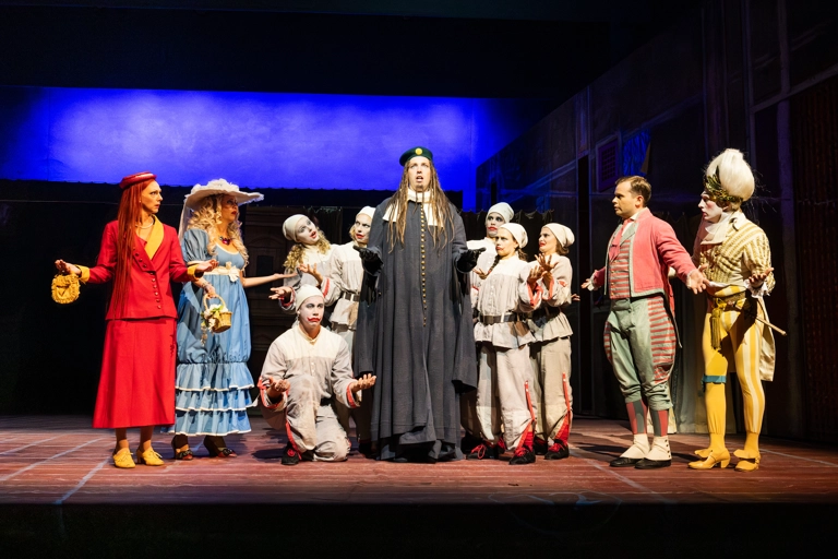Alidoro står och sjunger mitt i en grupp, inklusive Clorina, Thisbe, Don Ramiro, Dandini och några clowner.
