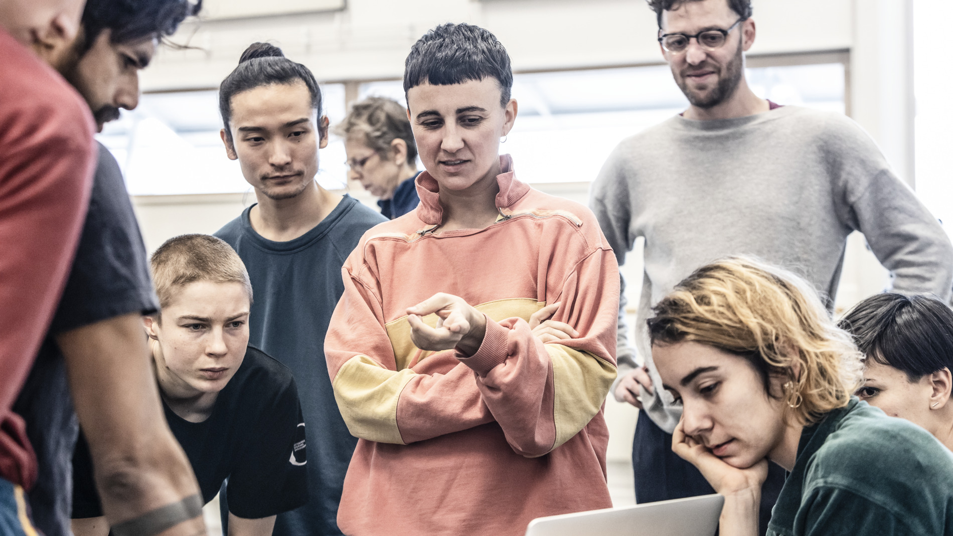 En grupp i en ljus dansrepetitionsstudio står tillsammans och tittar på en öppen laptop.