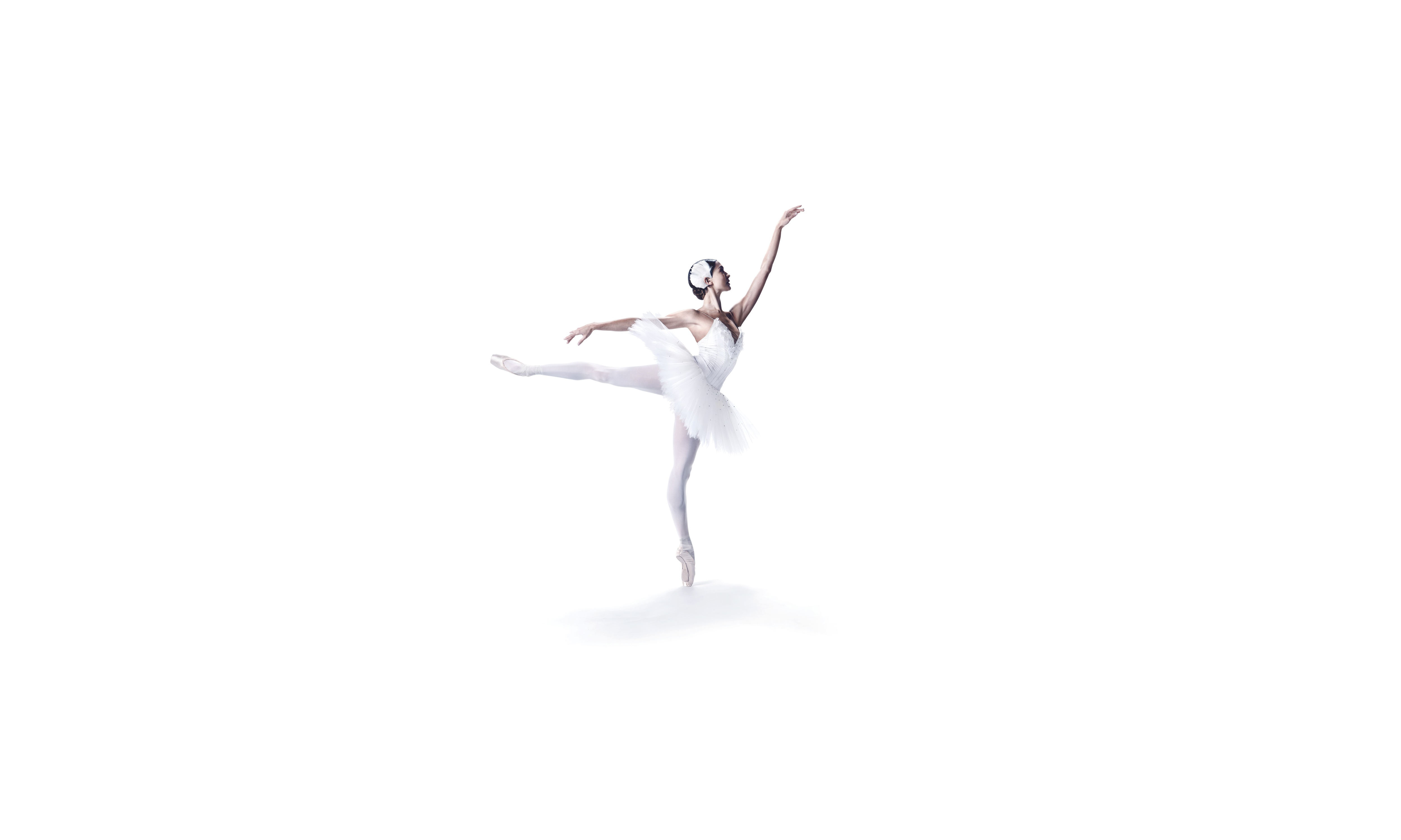 En ballerina i vit tutu balanserar på ena tån med en arm sträckt fram och ett ben utsträckt bakom sig.