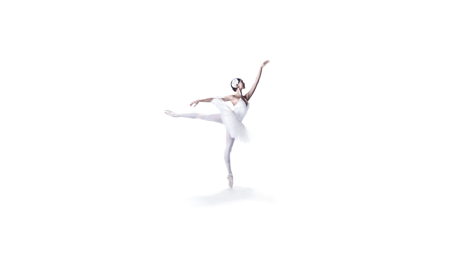 En ballerina i vit tutu balanserar på ena tån med en arm sträckt fram och ett ben utsträckt bakom sig.