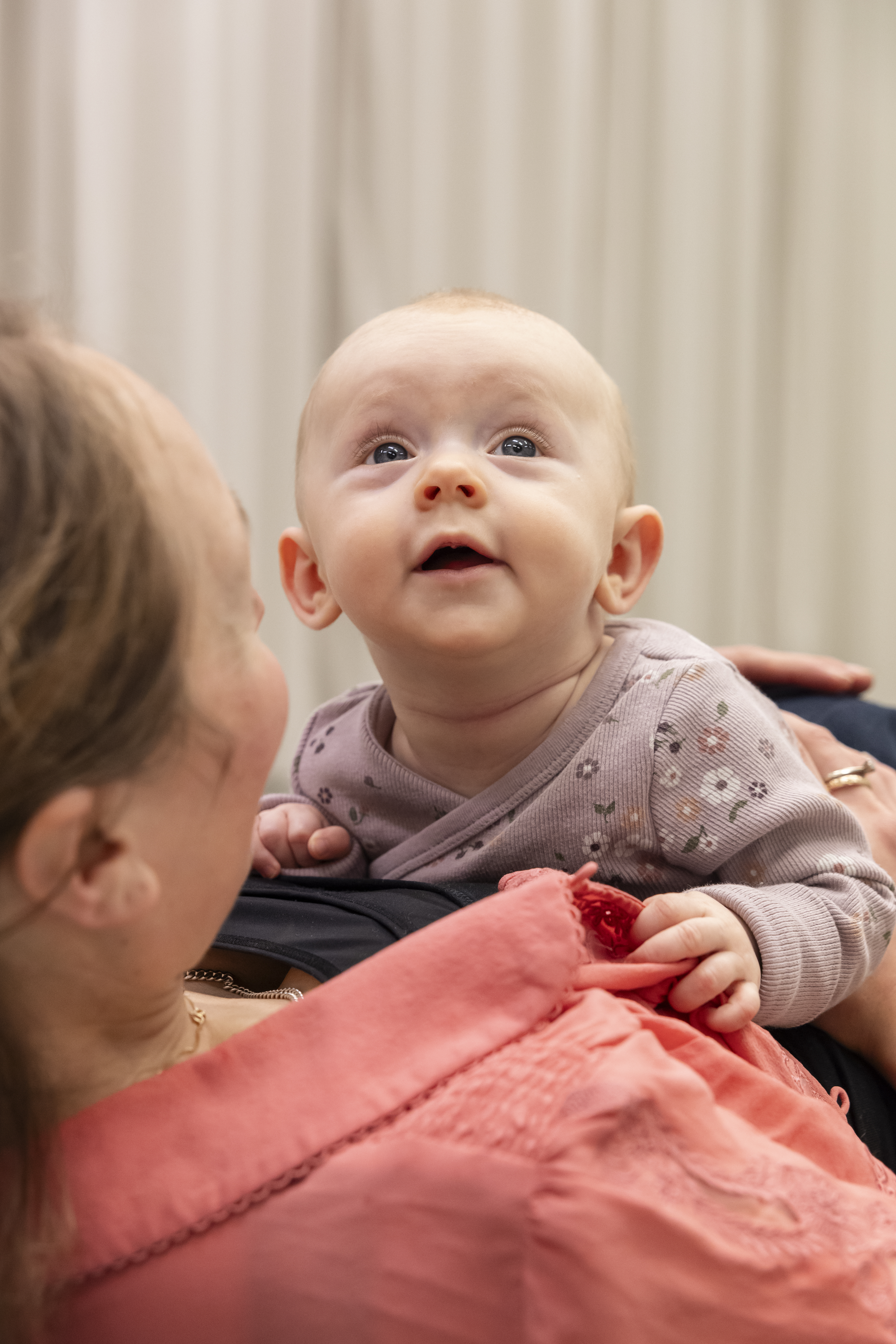 En ung bebis ligger på mage och tittar upp, med mage mot sin mamma. Mamman tittar på henne.