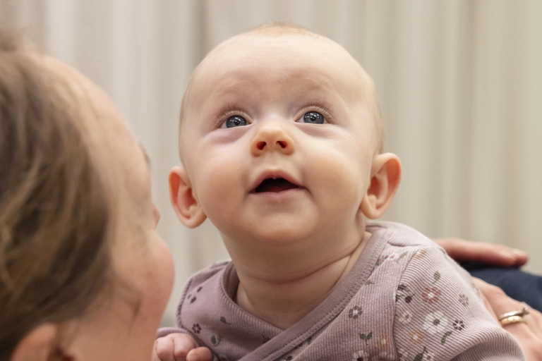En ung bebis ligger på mage och tittar upp, med mage mot sin mamma. Mamman tittar på henne.